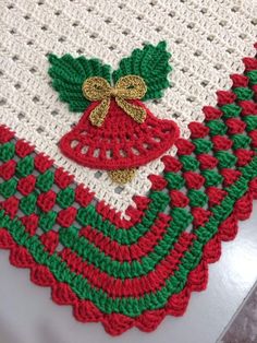 a crocheted table cloth with bells and holly leaves on the edge, sitting on a white surface