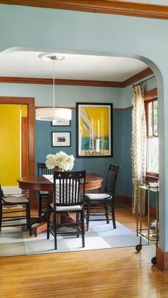 a dining room with blue walls and wood flooring is seen through an arch in the hallway