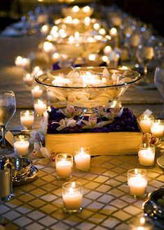 a long table with many lit candles and wine glasses on the side, along with other items