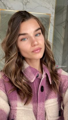 a woman with long hair and blue eyes is wearing a purple checkered coat in front of a marble wall