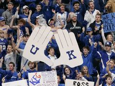 fans holding up signs in the stands at a football game, with one hand raised above their head