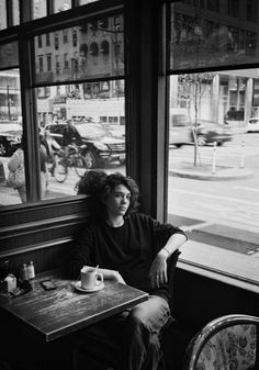 a man sitting at a table in front of a window with a cup on it