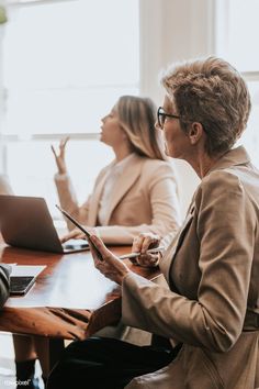 three women sitting at a table with laptops and papers in front of their faces