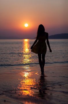 a woman walking on the beach at sunset