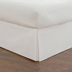 a bed with white sheets on top of it and wood floors in front of it