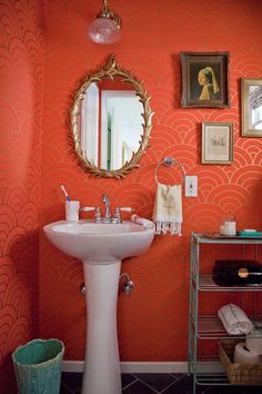 a bathroom with an orange wall and white pedestal sink in front of a round mirror