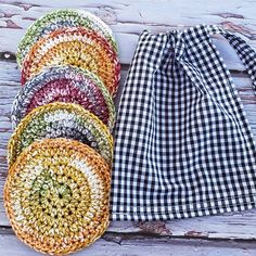 four crocheted dishcloths are sitting on a wooden table next to a black and white checkered cloth