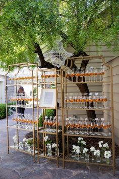 an outdoor bar with wine glasses and flowers on the shelves next to a large tree