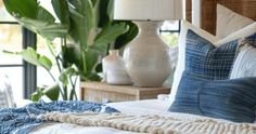 a bed with blue and white pillows on top of it next to a potted plant