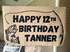 a man holding up a sign that says happy 12th birthday tanner on the side of his house