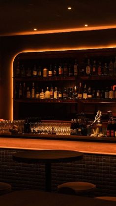 a dimly lit bar with liquor bottles on the shelves and stools in front of it