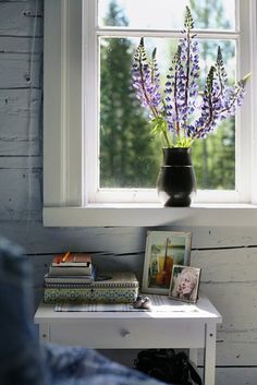 purple flowers in a black vase sitting on a white table next to a book shelf