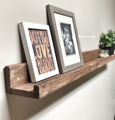 two framed pictures sitting on top of a wooden shelf next to a potted plant