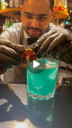 a man in gloves is making a cocktail at a bar with a blue drink and garnish on the rim