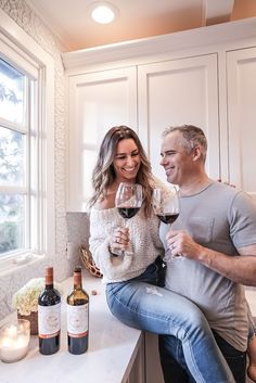 a man and woman sitting on a counter holding wine glasses