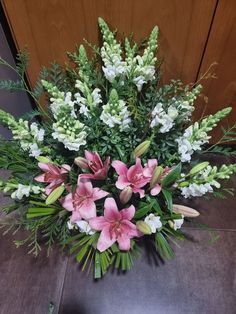 a vase filled with pink and white flowers sitting on top of a table next to a wooden door