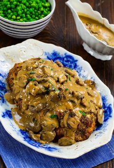 a blue and white plate topped with meat covered in mushroom gravy next to peas