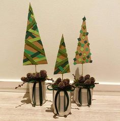 three vases with christmas trees in them sitting on a wooden floor next to a wall