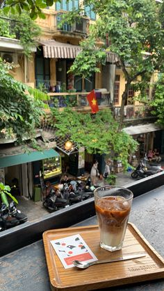 a drink sitting on top of a wooden tray next to a window filled with green trees