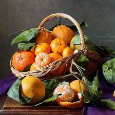 a basket filled with lots of oranges on top of a wooden table next to green leaves