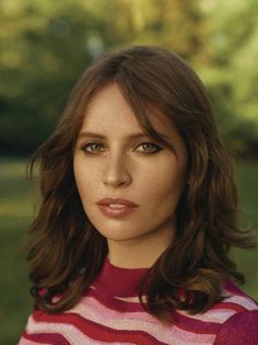 a close up of a person with long hair and wearing a striped sweater in a park