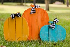 three wooden pumpkins sitting in the grass with black and white bows on their heads