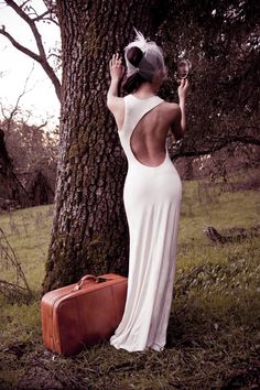 a woman standing next to a tree holding a wine glass in her hand and wearing a white dress