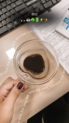 a person holding a cup of coffee in front of a keyboard