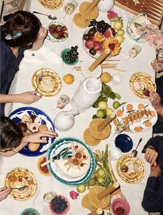 a group of people sitting around a table with plates and bowls on it, eating food