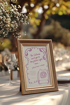 a table topped with a framed sign next to a vase filled with flowers