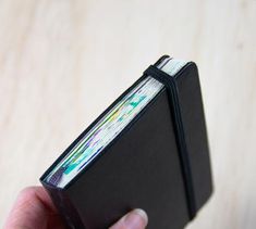 a hand holding an open black book on top of a wooden table