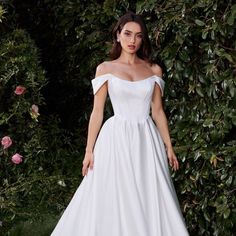 a woman in a white wedding dress standing next to some bushes and pink rose bush