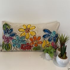 a decorative pillow with colorful flowers on it next to two potted succulents