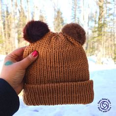 a hand holding a brown knitted hat with two pompoms