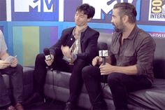 two men sitting on a couch talking to each other with microphones in front of them