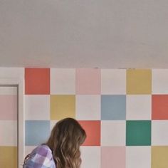 a woman standing in front of a wall with colorful squares painted on it and holding a remote control