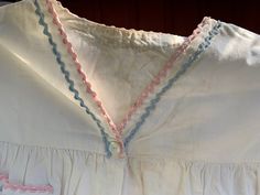 "An old nightshirt nightgown made of white cotton with pastel pink and blue rick rack trim around cuffs, pocket and V neckline. It has two shell buttons at center front. Skirt is gathered into yoke at the underarms. ¾ sleeves have no fullness at shoulder. Fabric is a heavier weight than quilting fabric. It's more like a very good quality bed sheet or pillowcase. This gown is shown on the left of the first and last photo. Approximate measurements when laid flat: 17.5\" between shoulders 44\" arou Cotton Daywear Dresses With Picot Trim, Cotton Dresses With Picot Trim For Daywear, Vintage Cotton Ruffled Sleepwear, Vintage Cotton Sleepwear With Ruffles, White Cotton Nightgown, Womens Lingerie, Cotton Nightgown, Rick Rack, Shell Buttons