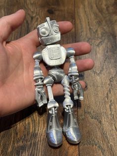 a hand holding a silver robot toy on top of a wooden table next to a person's hand