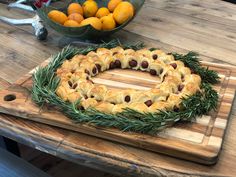 an olive wreath on a cutting board with oranges in the bowl and other food