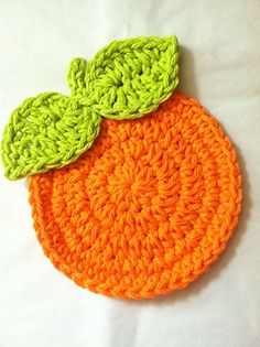 an orange crocheted coaster with green leaves