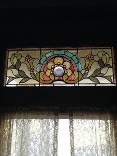 a stained glass window in the corner of a room with sheer curtains and drapes