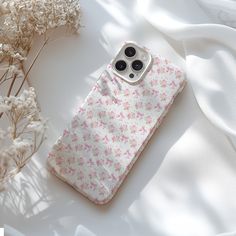 an iphone case sitting on top of a white surface next to flowers and a plant