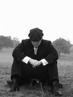 an old man sitting in the grass with his hands on his knees