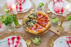 a pizza sitting on top of a wooden table next to plates and glasses filled with drinks