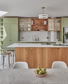 a kitchen with green cabinets and white chairs, an island countertop has pears on it