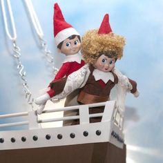 two elf dolls are sitting on top of a boat with chains hanging from it's sides