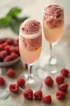 two wine glasses filled with ice cream and raspberries on a table next to berries