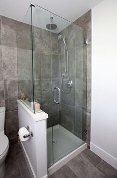 a bathroom with a glass shower door and toilet in the corner, next to a tiled wall