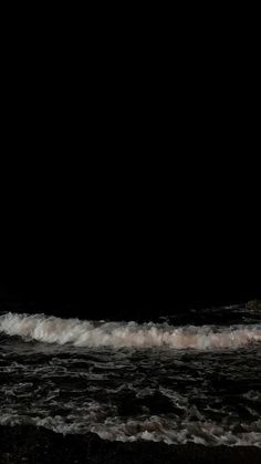 a man standing on top of a surfboard next to the ocean in the dark