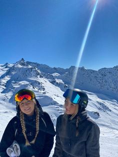 two women standing on top of a snow covered slope wearing skis and goggles